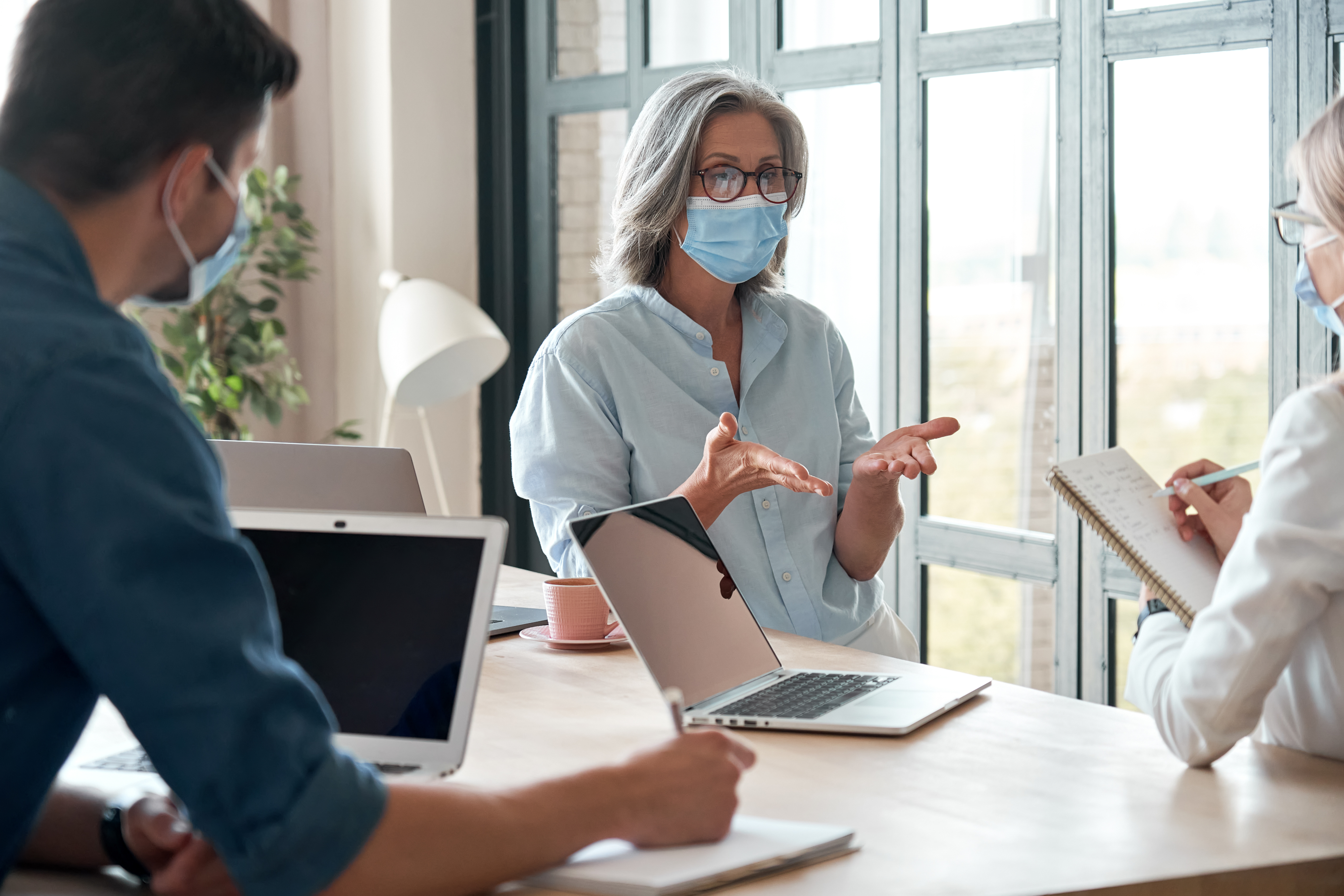 Drei Mitarbeitende tragen einen medizinischen Mund-Nasen-Schutz und diskutieren in einem hellen Büro