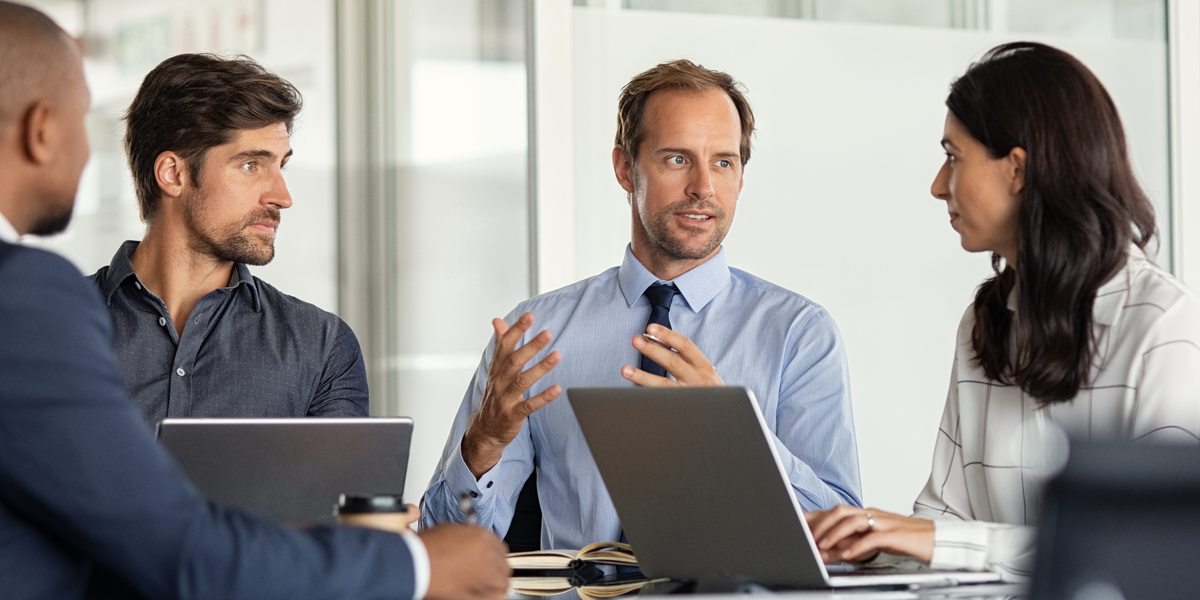 Drei Männer und eine Frau in einem Meeting, Laptops und Unterlagen auf dem Tisch