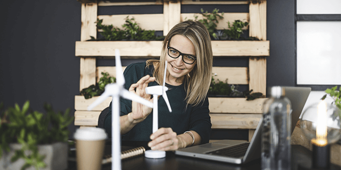 Junge Frau in minimalistischem Büro mit vielen Grünpflanzen betrachtet Windradmodell