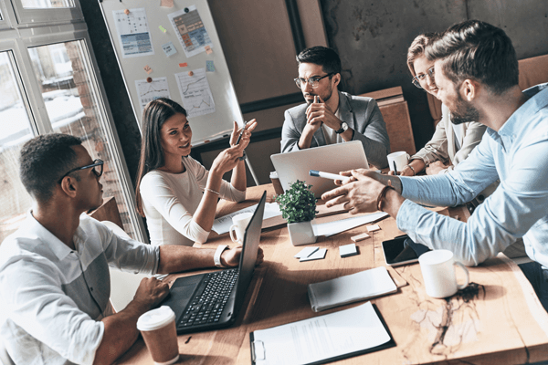 Diverses Team in Meeting mit Tisch, Laptops, Unterlagen und Magnetwand diskutiert