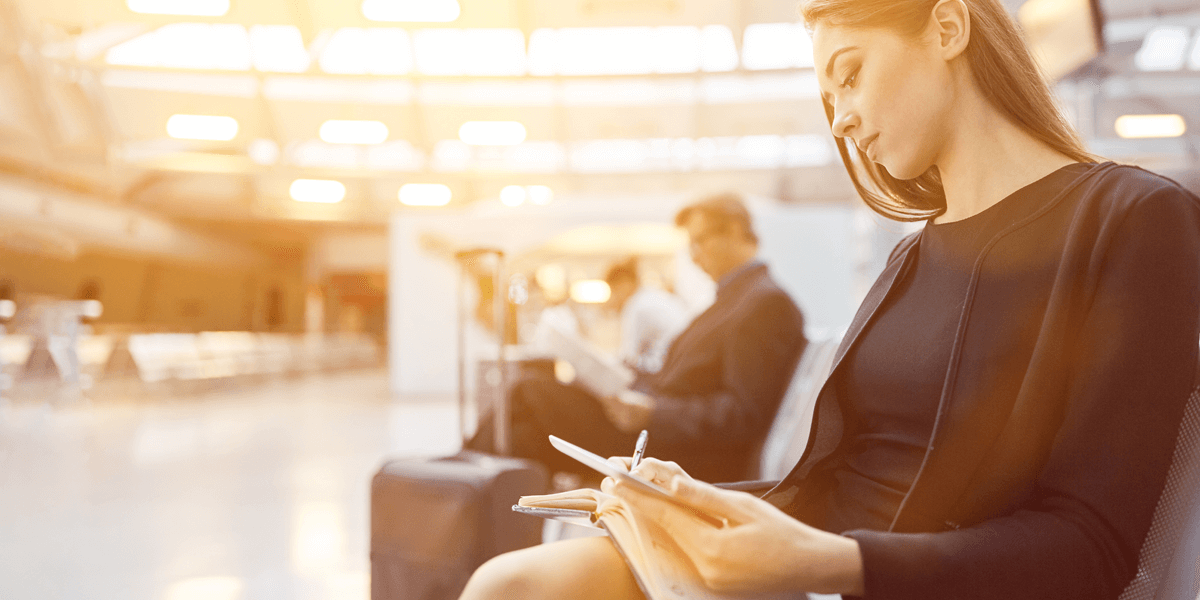 Junge Geschäftsfrau sitzt im Wartebereich eines Flughafens und macht Notizen in ihrem Terminkalender 