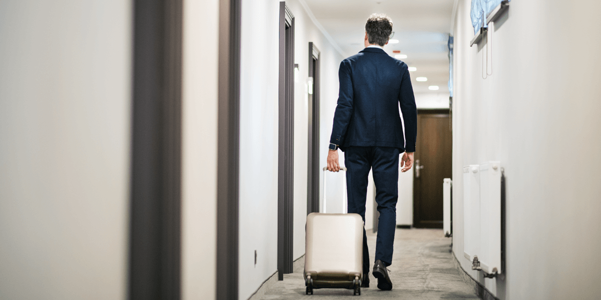 Rückenansicht auf Geschäftsmann mit Koffer auf Dienstreise geht durch Hotelkorridor 