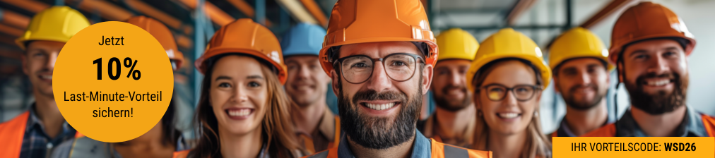 Gruppe mit Schutzhelmen steht in einer Industriehalle und blickt nach vorn